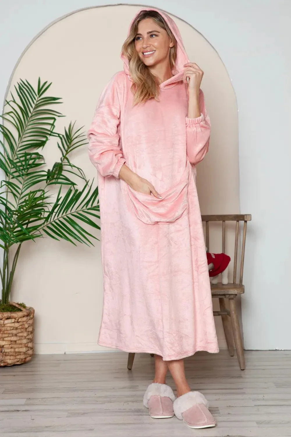 woman wearing pink hooded midi lounge dress with full-size pockets and slippers indoors
