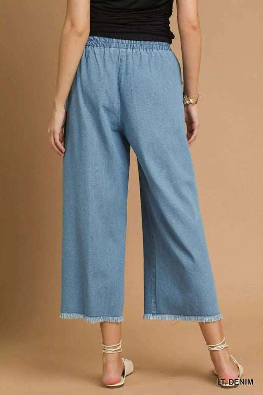 Rear view of Umgee washed fringe hem wide leg light denim jeans with elastic waistband and raw hem fringe detailing