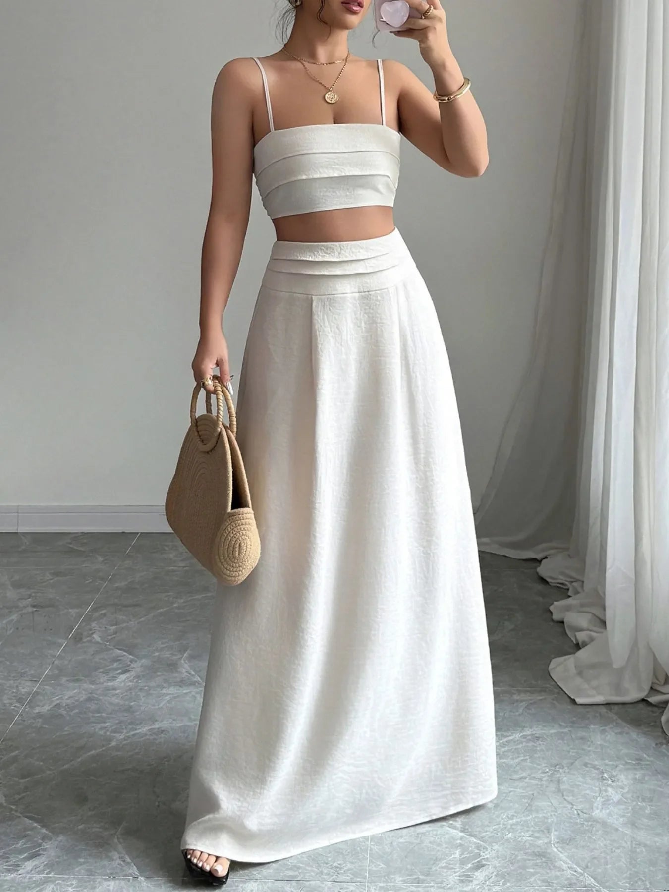 Woman wearing white square neck cami with ruched detail and matching maxi skirt set holding a woven handbag indoors