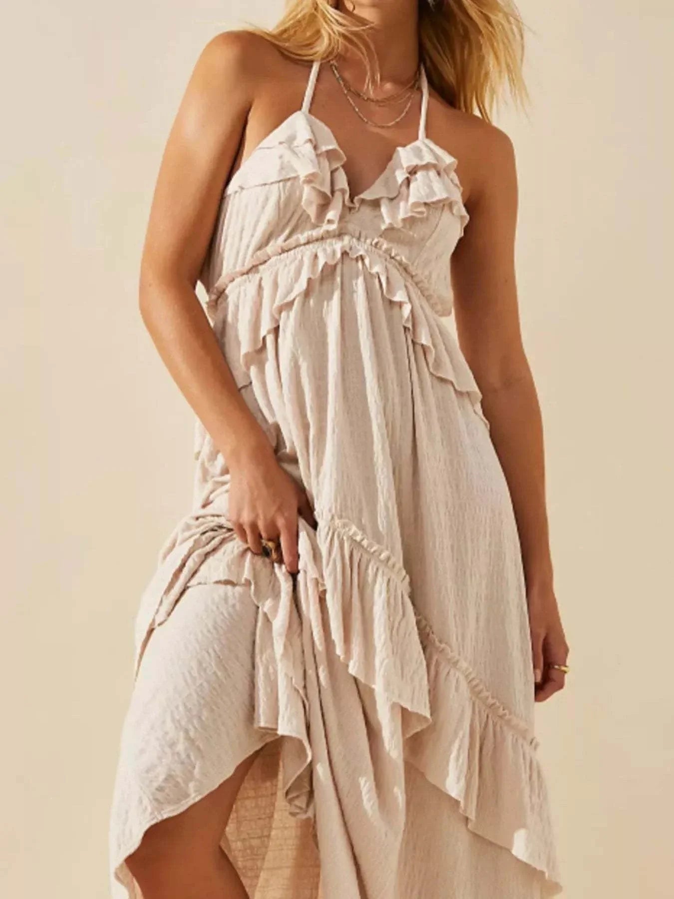 Woman wearing a beige ruffled halter neck maxi dress with tied straps and layered ruffle details
