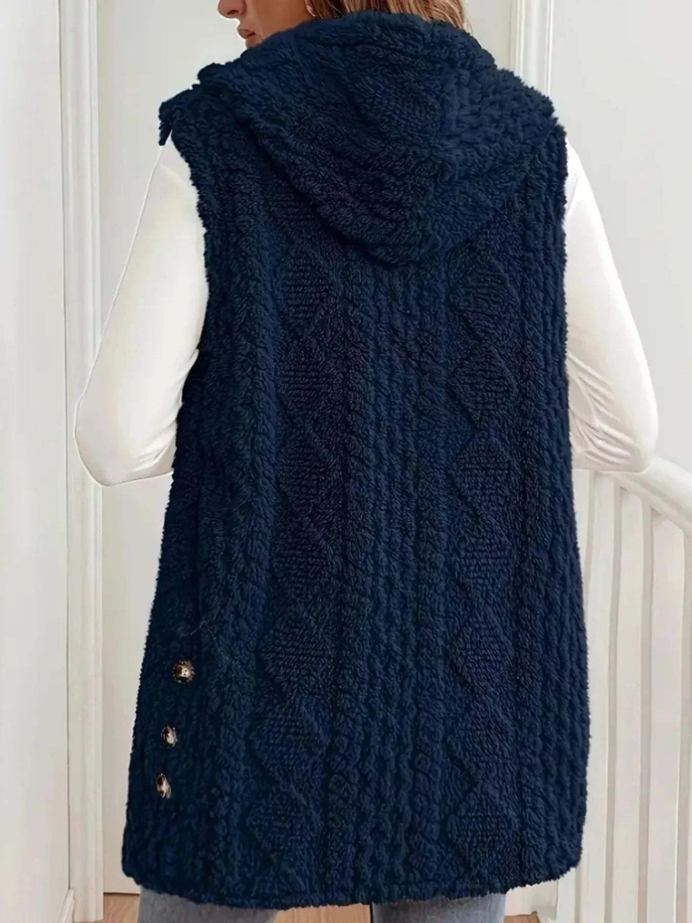 Back view of navy blue button up plush hooded vest with textured knit pattern and side buttons worn over white long sleeves