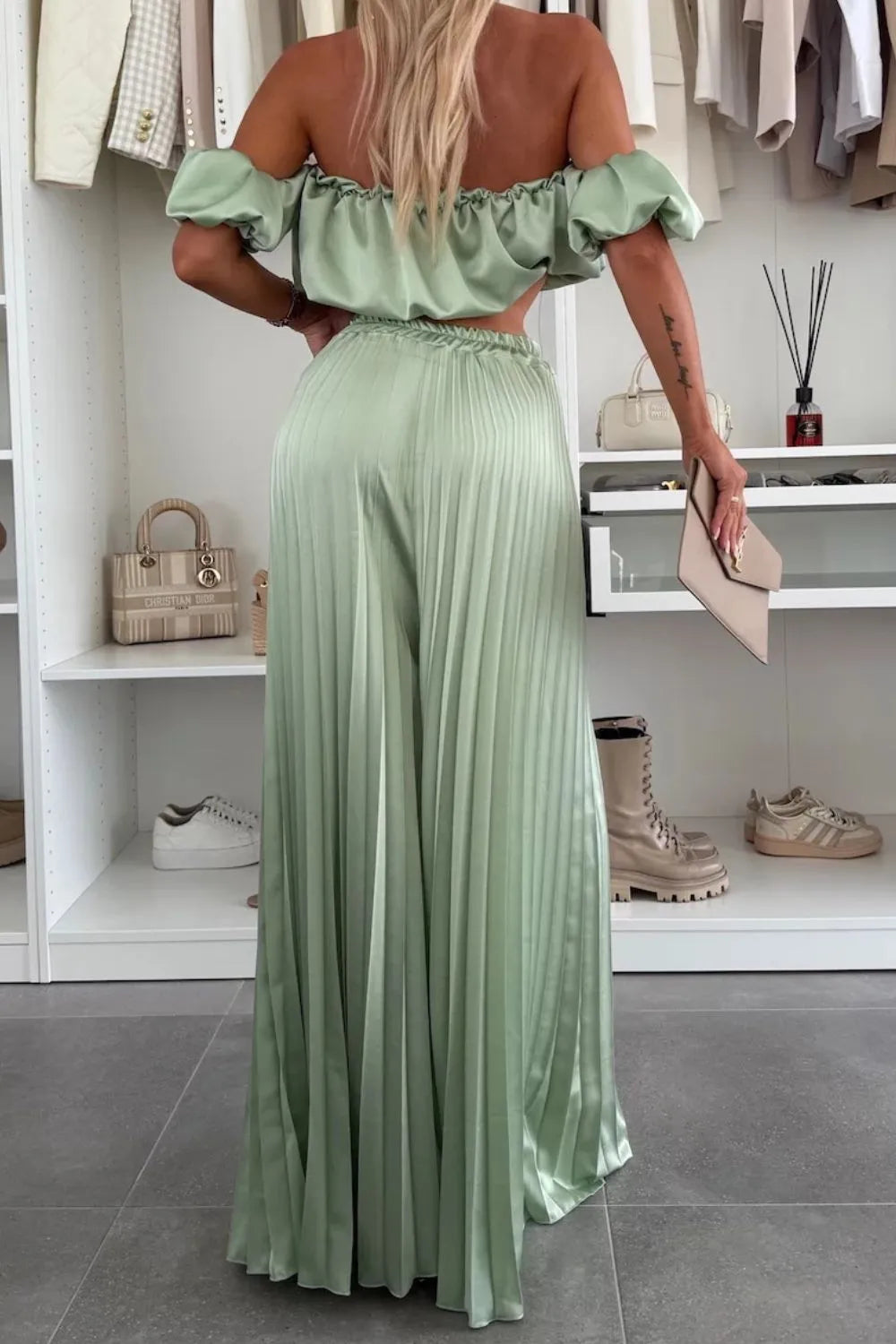 Woman wearing green off-shoulder ruffled top and pleated pants set back view
