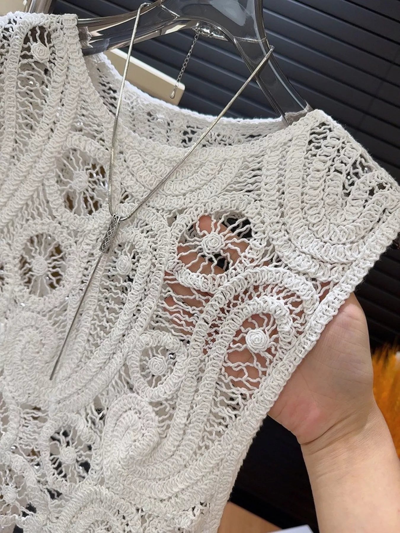 Close-up of white crochet sleeveless tank with openwork pattern and necklace on hanger