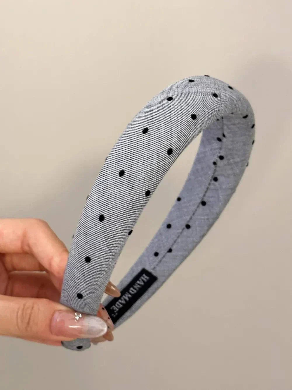 Polka dot polyester wide headband with black dots on grey background held in hand