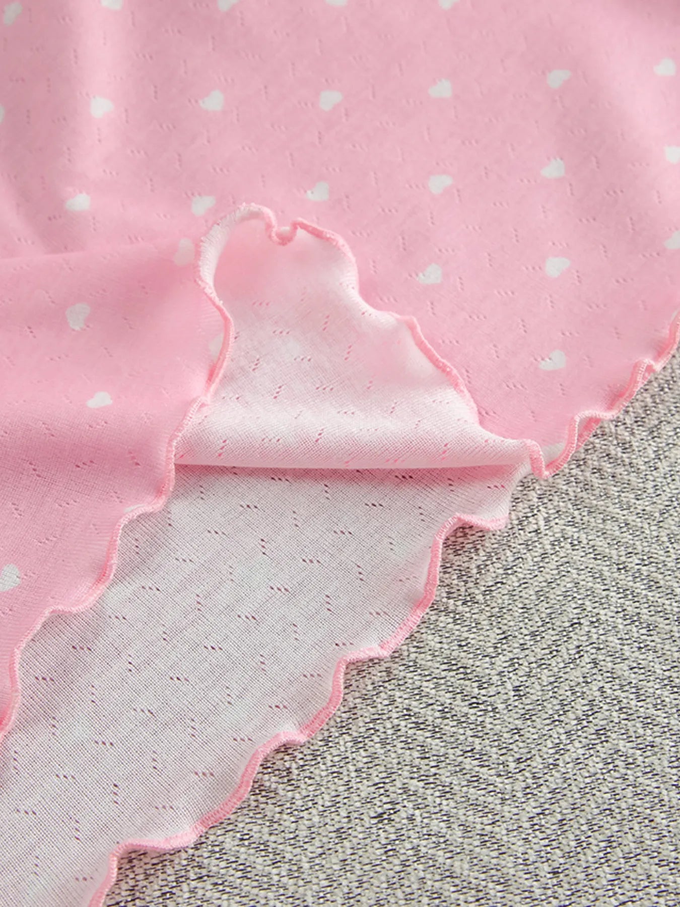 Pink polka dot round neck top fabric with ruffled edge detail close-up