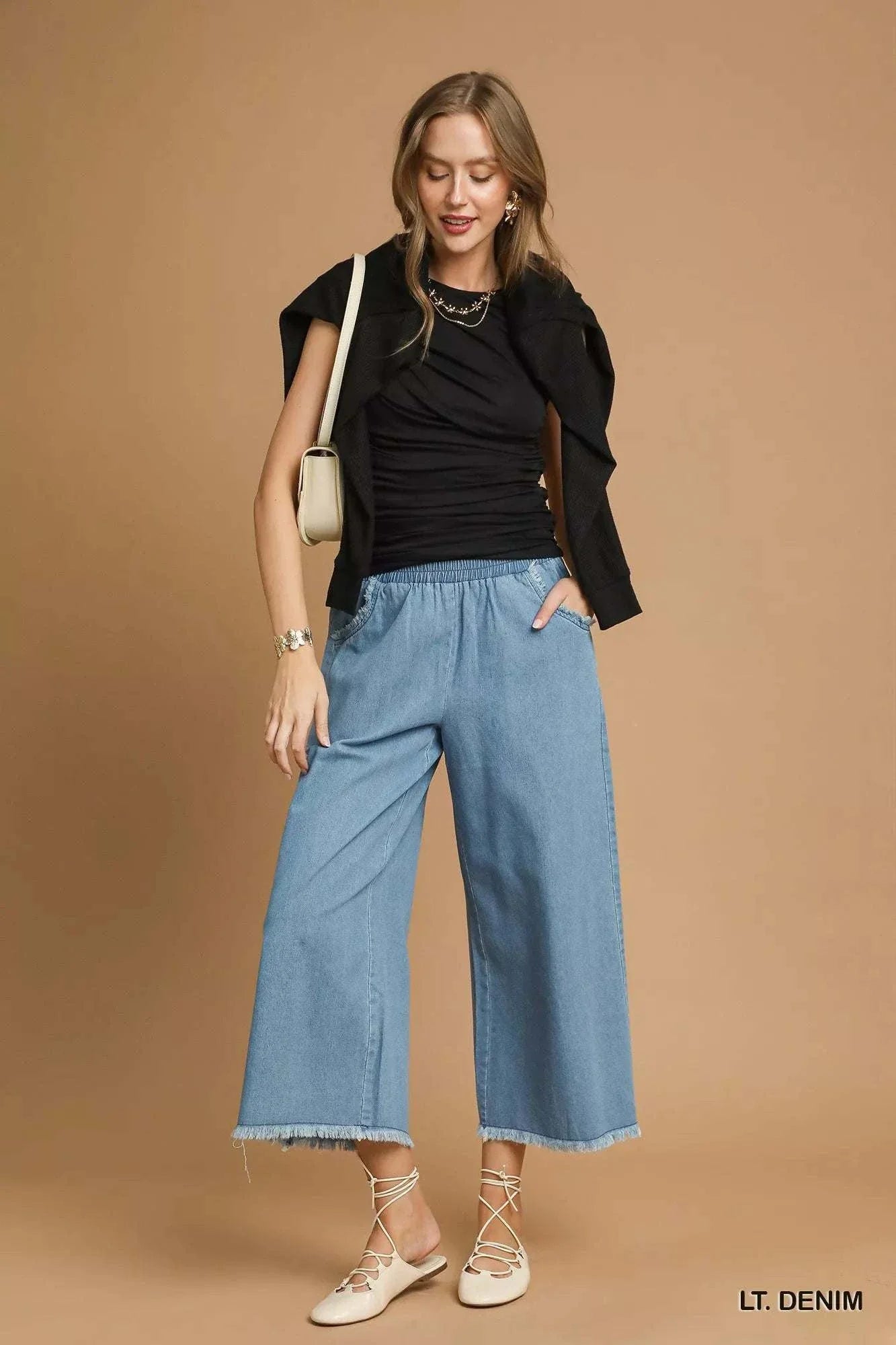 Woman wearing Umgee washed fringe hem wide leg jeans in light denim with elastic waistband and side pockets