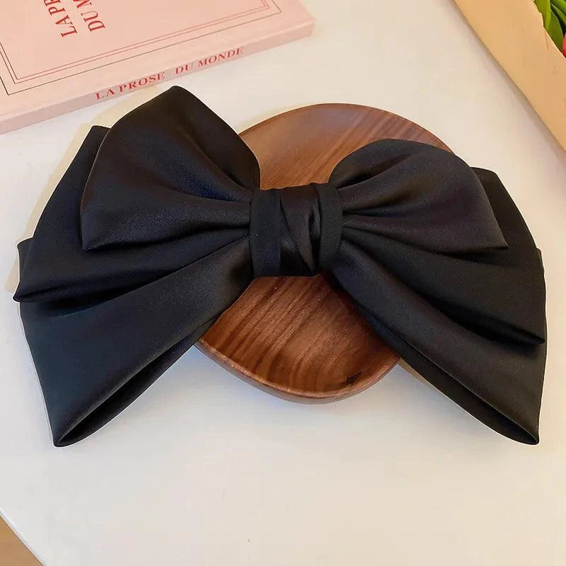 Black bow cloth hair clip made of cloth and alloy with large bow design on wooden plate