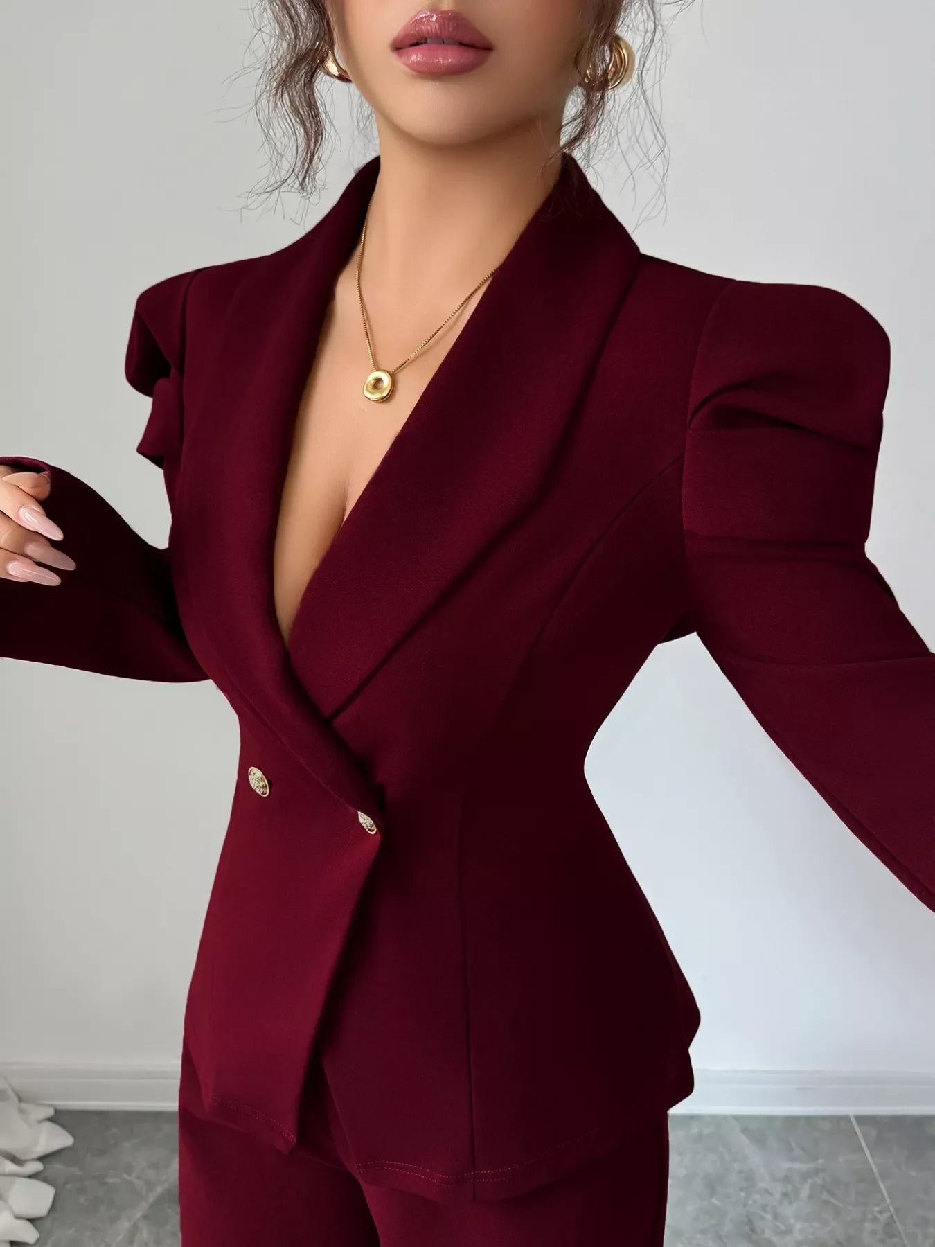 Woman wearing a burgundy double-breasted blazer and pants suit set with gold buttons and puffed shoulders