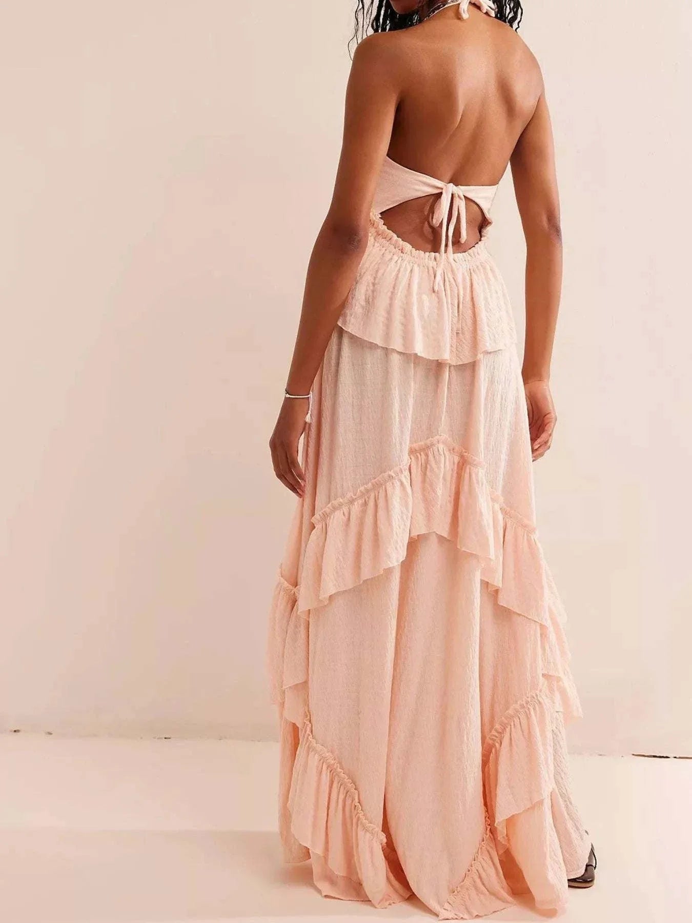 Back view of a peach ruffled halter neck maxi dress with tied open back and tiered skirt design