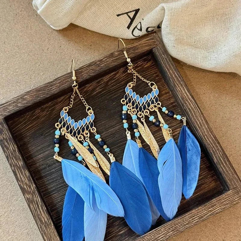 Blue feather and rice bead alloy dangle earrings on wooden tray